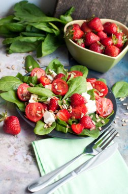 Çilekli salata, kiraz domatesleri, ayçekirdeği, ıspanak ve gri arka planda beyaz peynir. Üst görünüm