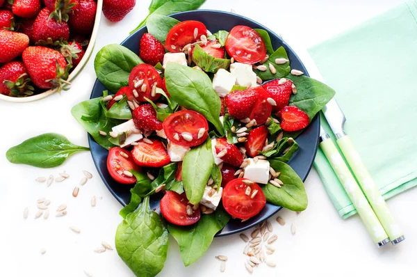 Salad with strawberries, cherry tomatoes, sunflower seeds, spinach and feta cheese on white background. Top view