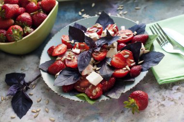 Çilekli salata, kiraz domatesleri, ayçekirdeği, fesleğen ve gri arka planda beyaz peynir.