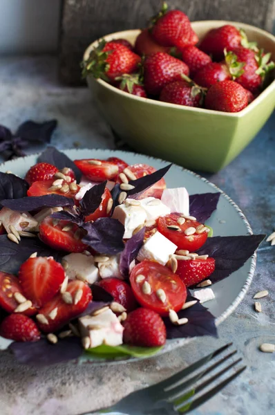 Salad with strawberries, cherry tomatoes, sunflower seeds, basil and feta cheese on gray background