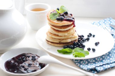 Çay, krep, taze yaban mersini ve beyaz arka planda naneli kahvaltı. Beyaz tabakta kızarmış krep..