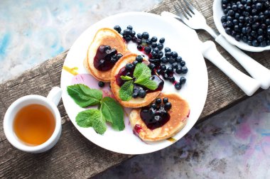 Çay, krep, taze yaban mersini ve ahşap masada naneli kahvaltı. Beyaz tabakta kızarmış krep. Üst görünüm