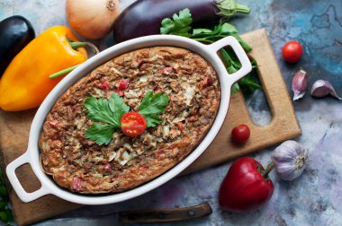 Ev yapımı patlıcan güveci, dolmalık biber, soğan, sarımsak, tahta tahtada maydanoz ve gri bir arka plan. Patlıcan güveci ve sebzeli güveç. Üst görünüm