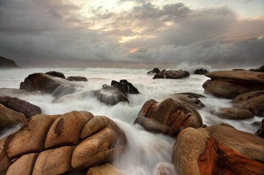 Ocean surges over weathered rocks clipart