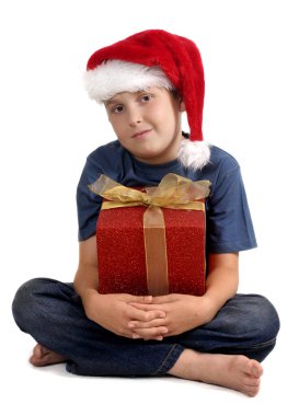 Mavi kot pantolon ve tişörtlü çapraz bacaklı çocuk elinde altın bir fiyonkla kırmızı bir hediye tutuyor. Beyaz arkaplan.