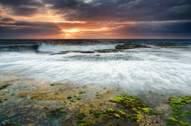 Narrabeen resifinde gelgit var. Güneş çizgili bulutlarla kayalık..