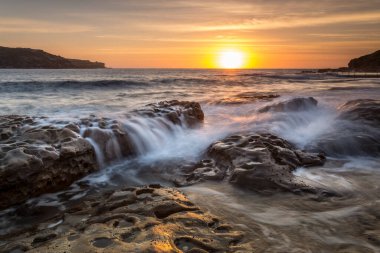 Ufukta yükselen güneş, altın ışığını Long Bay 'den Malabar' a kadar ön planda kaya akıntılarıyla parlıyor..