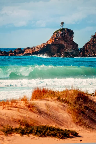 Dalgalar kıyı şeridine çarparken tek bir kayanın üzerindeki ilk güneş ışığı