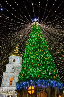 Büyük dekore edilmiş Noel ağacı, parlak gölgelik ışıkların altında geceleri parlıyor neşeli bir bayram kutlaması ve büyülü bir kış hissi yaratıyor. Ana Kyiv 'in Yeni Yıl ağacı ve arka planda Aziz Sophia Katedrali.