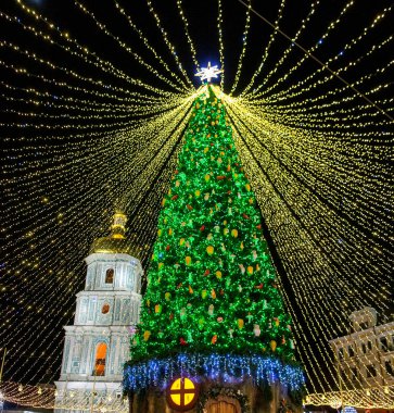 Büyük dekore edilmiş Noel ağacı, parlak gölgelik ışıkların altında geceleri parlıyor neşeli bir bayram kutlaması ve büyülü bir kış hissi yaratıyor. Ana Kyiv 'in Yeni Yıl ağacı ve arka planda Aziz Sophia Katedrali.