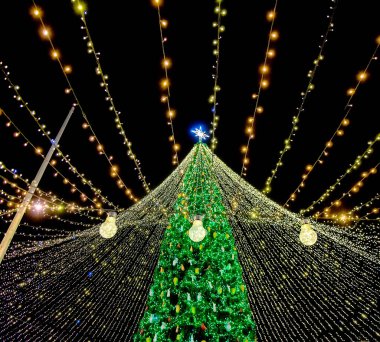 Parlak noel ışıkları ve yıldızın önünde parlayan ampuller asılı. Büyülü bayram gecesi atmosferi yaratıyor.