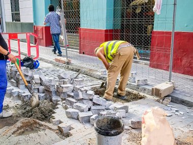 İnşaat işçileri kaldırımdaki taş blokları değiştirerek, el emeği ve kentsel altyapı onarım sürecini gösteriyor
