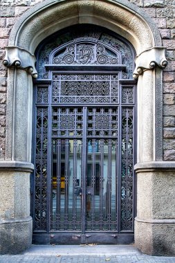 Dekoratif dövmeli demir kapı. Taş kemer çerçeveli. Detaylı metal işleme kalıpları ve katı tarihi kentsel mimari tasarımı var.