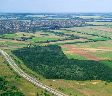 Yoğun orman tarlaları ve kırsal yolları gösteren eğimli hava manzarası orman ve ekili arazi arasında güçlü bir zıtlık yaratıyor.