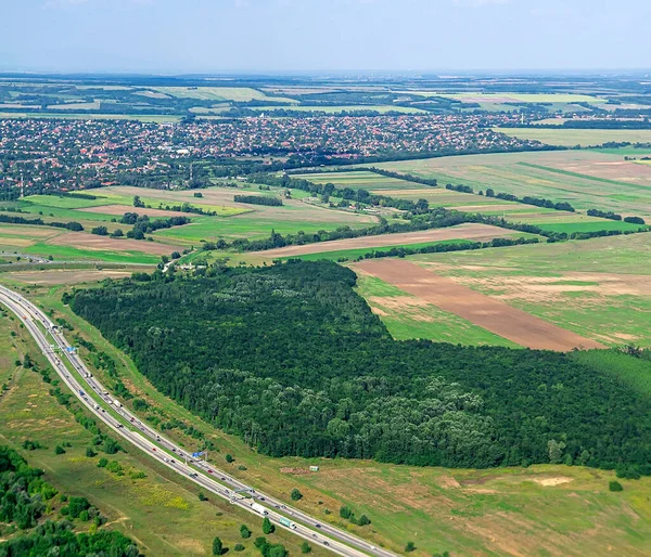 Yoğun orman tarlaları ve kırsal yolları gösteren eğimli hava manzarası orman ve ekili arazi arasında güçlü bir zıtlık yaratıyor.