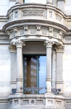 Korint sütunları, karmaşık taş oymaları ve tarihi bir cepheye işlenmiş demir korkulukların yer aldığı süslü klasik koy penceresinin ayrıntılı görüntüsü. Lüks gayrimenkul, mimari miras ve kentsel tasarım uygulamaları için ideal.