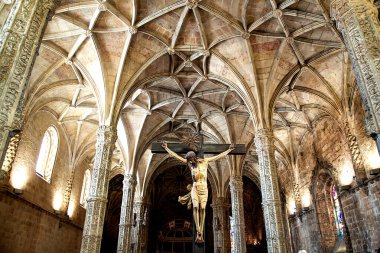 Portekiz, Lizbon - 05 Ağustos 2018: Jeronimos Manastırı 'nda UNESCO' daki Gotik-Manueline kemerlerinin altında çarmıha gerilen karmaşık kaburgalı tuğlalar, süslü taş sütunlar ve merkezi altın İsa heykellerini gösteren dramatik manzara