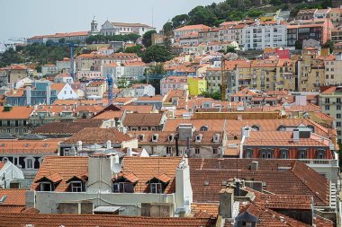 Turuncu-kırmızı terracotta çatıları, pastel cepheler, bacalar, yeşil ağaçlar ve açık bir gökyüzünün altında Lizbon tepelerine tırmanan dağınık modern yapılara tepeden bakan yüksek görüş açısı. Yüksek kalite fotoğraf.