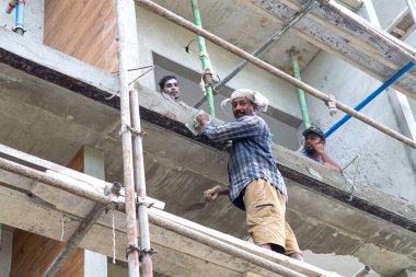 Maldivler, Thoddoo - 22 Şubat 2022: Gündelik iş kıyafetleri içinde koyu tenli iki erkek işçi, bina bitirme işi ile meşgul, biri fırçayla duvara boya sürme, diğeri ise beyaz cephelere karşı iskele destekleme, tropikal göstergeler