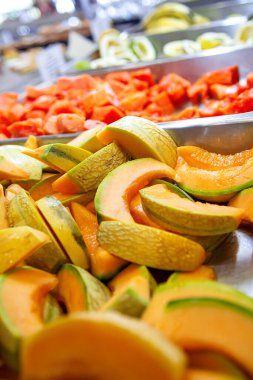 Hotel buffet fruit station in Dominican Republic resort featuring large trays of fresh chopped papaya chunks, cantaloupe wedges, green melon slices and assorted tropical fruits with serving tongs. Captures authentic vibrant healthy tropical selection