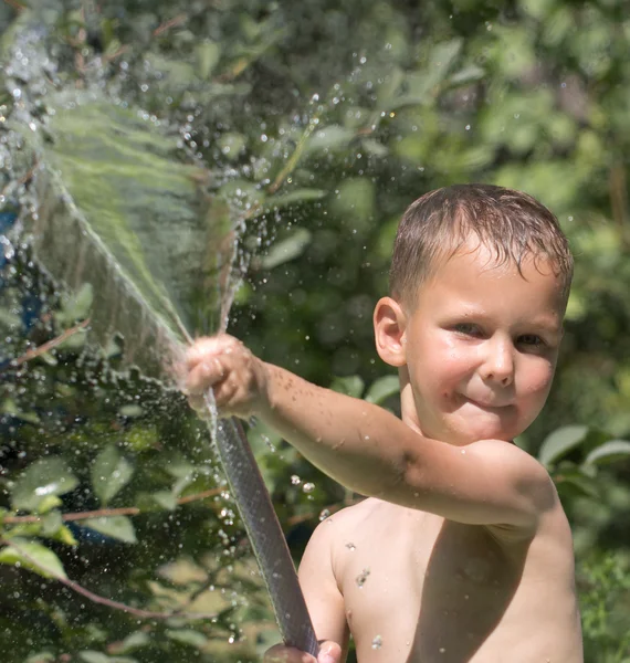 Chlapec stříkat vodu z hadice — Stock fotografie