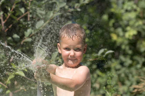 Chlapec stříkat vodu z hadice — Stock fotografie