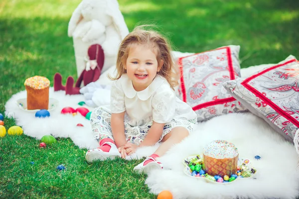 Criança feliz senta-se em um prado em torno da decoração de Páscoa — Fotografia de Stock