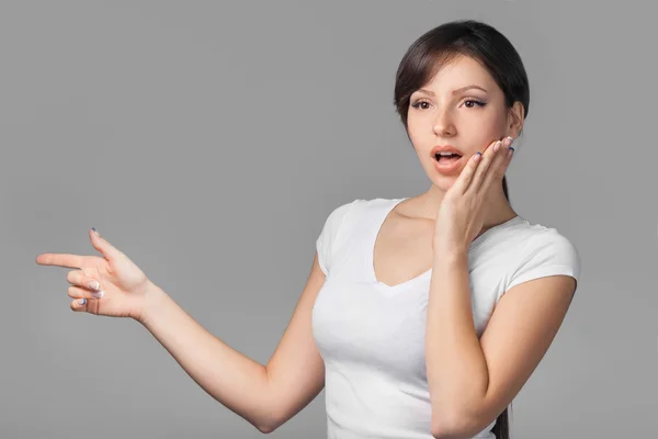 Junge überraschte Frau zeigt mit dem Finger Leerstelle auf grauem Hintergrund — Stockfoto