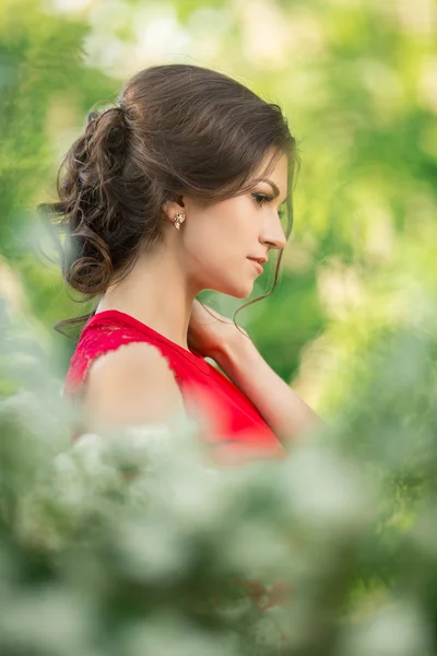 Schöne junge brünette Frau, die in der Nähe weißer Blüten steht — Stockfoto