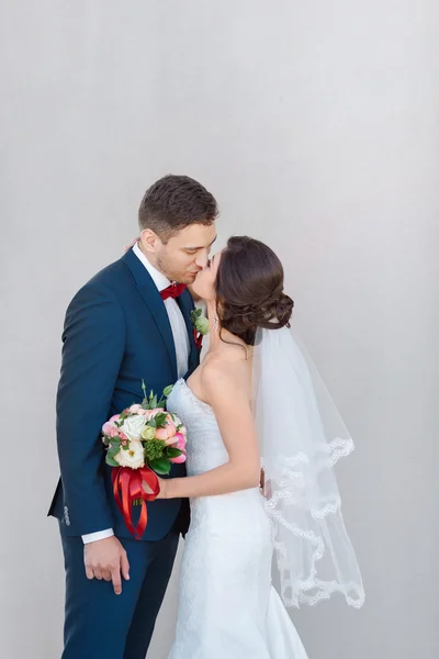 Unga bröllop par kyssar mot en grå vägg — Stockfoto