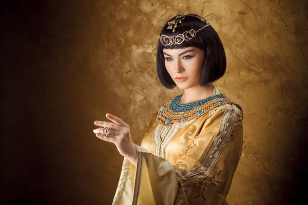Beautiful Egyptian woman like Cleopatra pointing finger away on golden background — Stock Image Beautiful Egyptian woman like Cleopatra pointing finger away on golden background Stock Photo