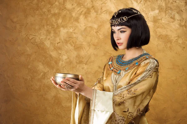 Beautiful woman like Egyptian Queen Cleopatra with cup on golden background — Stock Image Beautiful woman like Egyptian Queen Cleopatra with cup on golden background Stock Image