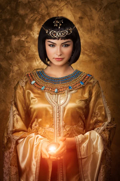 Mooie Egyptische vrouw zoals Cleopatra met magische bal op gouden achtergrond — Stockfoto