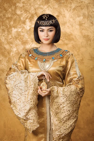 Hermosa mujer egipcia como Cleopatra con frasco de perfume sobre fondo dorado —  Fotos de Stock