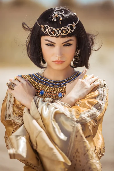 Bella donna con trucco di moda e acconciatura come la regina egiziana Cleopatra all'aperto contro il deserto tempo ventoso Fotografia Stock