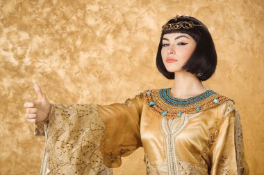 Kleopatra gibi ciddi Mısırlı kadın başparmak yukarı jest ile, altın arka plan üzerinde