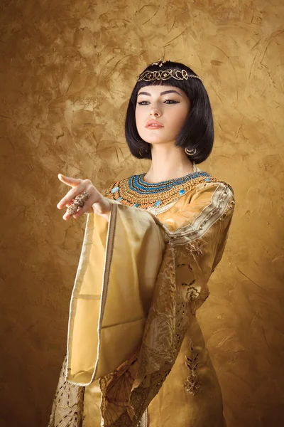 클레오 파트라 같은 아름다운 이집트 여자는 황금 배경에 멀리 손가락을 가리키는 — 스톡 사진