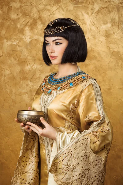 Krásná žena jako egyptská Královna Kleopatra s cup na zlatém pozadí — Stock fotografie