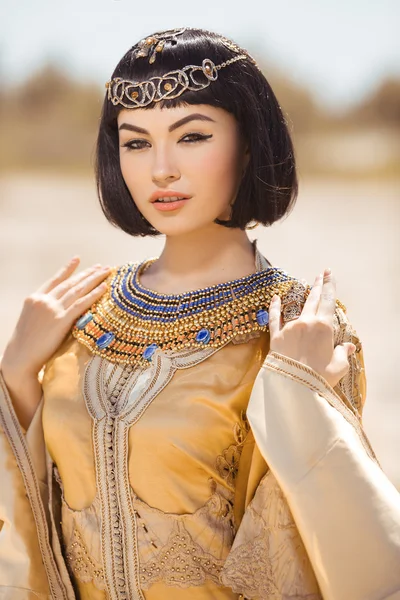 Beautiful woman with fashion make-up and hairstyle like Egyptian queen Cleopatra outdoors against desert — Stock Image Beautiful woman with fashion make-up and hairstyle like Egyptian queen Cleopatra outdoors against desert Stock Picture