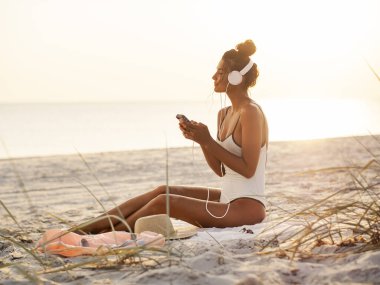 Bikini 'deki kumsalda akıllı telefonu ve kulaklığı olan kadın.