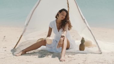 Kadın sahilde dinlenirken hindistan cevizi suyu içiyor.