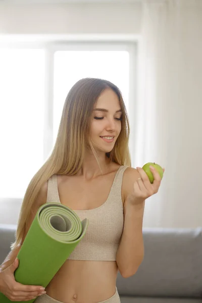Женщина с ковриком для йоги и яблоком дома — стоковое фото