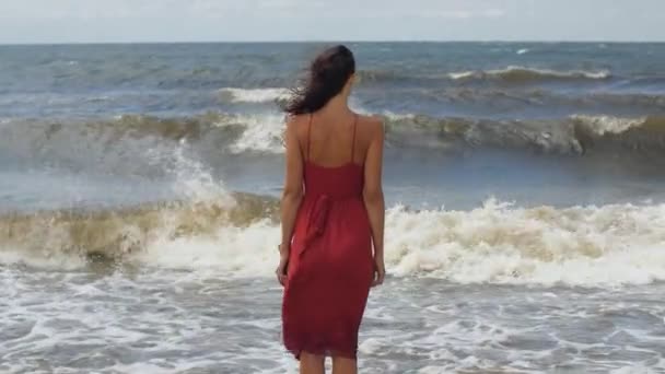 Γυναίκα σε ένα κόκκινο στην παραλία, κρύος άνεμος καιρός — Αρχείο Βίντεο
