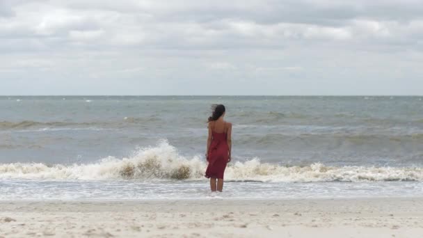 Vrouw in het rood op het strand, koud weer — Stockvideo