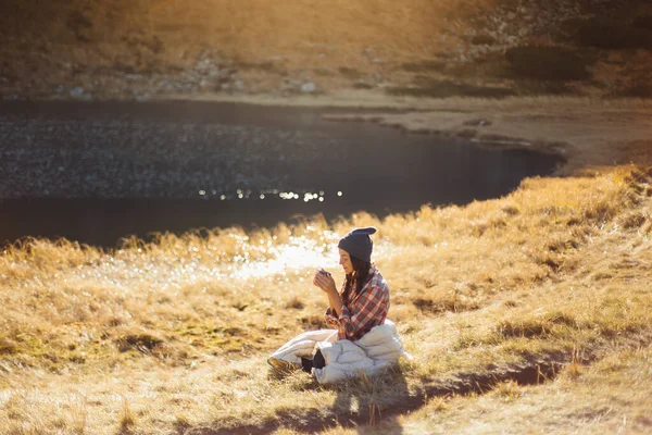 湖の近くのコーヒーカップで山の中を歩く旅行者の女性 — ストック写真