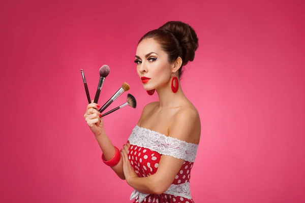 Woman with makeup brushes.   She is standing against a pink background. — Stock Photo, Image