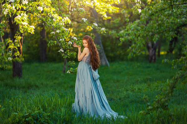 Beautiful pregnant woman smells blossom, outdoor in nature