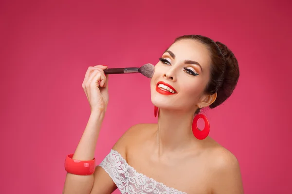 Smiling Woman with makeup brush. She is standing against a pink background. — Stock Photo, Image