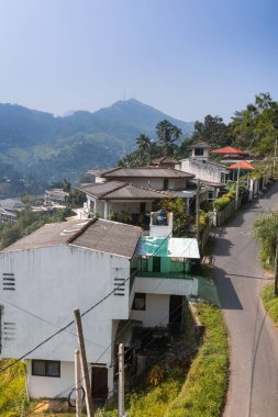 Kandy, Sri Lanka 'da arka planda dağ manzaralı konutların bulunduğu pitoresk bir yamaç sokağı. Bu sakin şehir manzarası seyahat, mimari ve kültürel turizm için idealdir.
