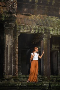 Beyaz bluzlu ve turuncu etekli genç kadın Angkor Wat, Kamboçya 'daki eski yosun kaplı tapınak kalıntılarını keşfediyor. Kaliteli seyahat, kültür turizmi ve yazı işleri için macera yaşam tarzı konsepti